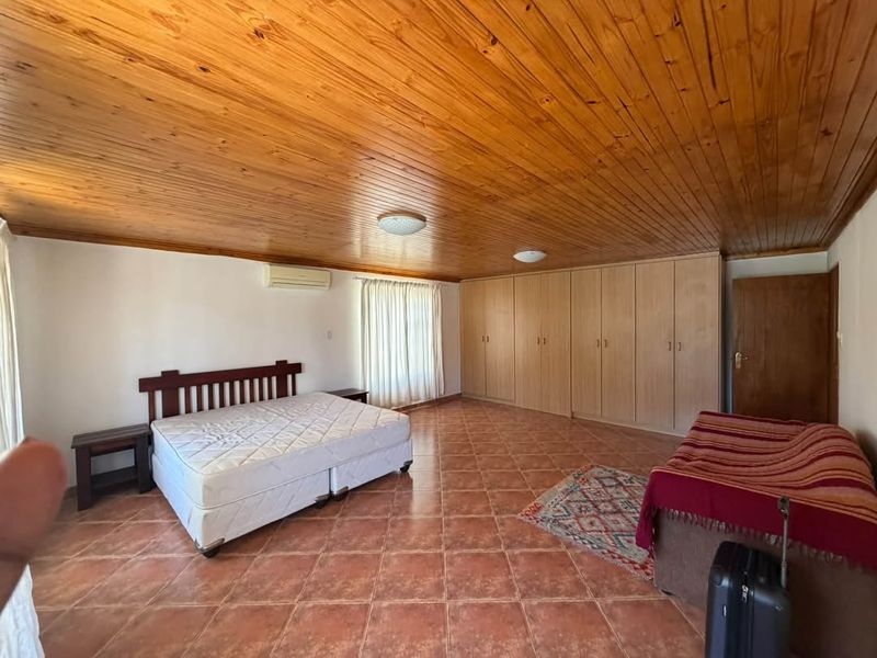 Spacious bedroom featuring a warm timber-clad ceiling, extensive built-in storage cupboards, tiled flooring, and a wall-mounted air conditioning unit.