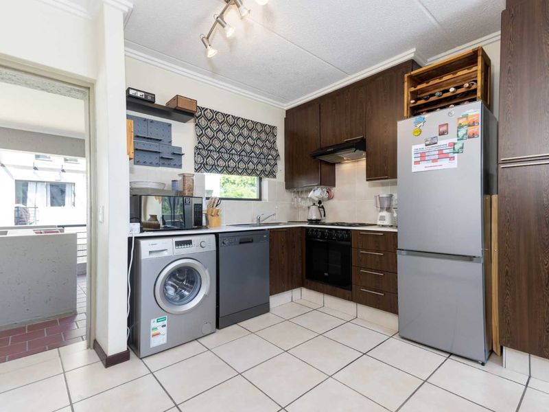 A functional kitchen featuring dark wood cabinetry, tiled flooring, a built-in oven with extractor fan, and a tiled backsplash.