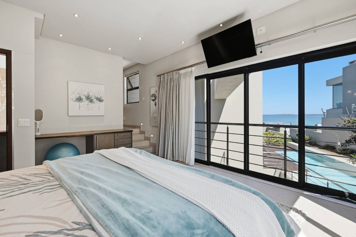 Modern bedroom featuring recessed lighting, a built-in desk, and large sliding glass doors opening to a balcony with pool and ocean views.