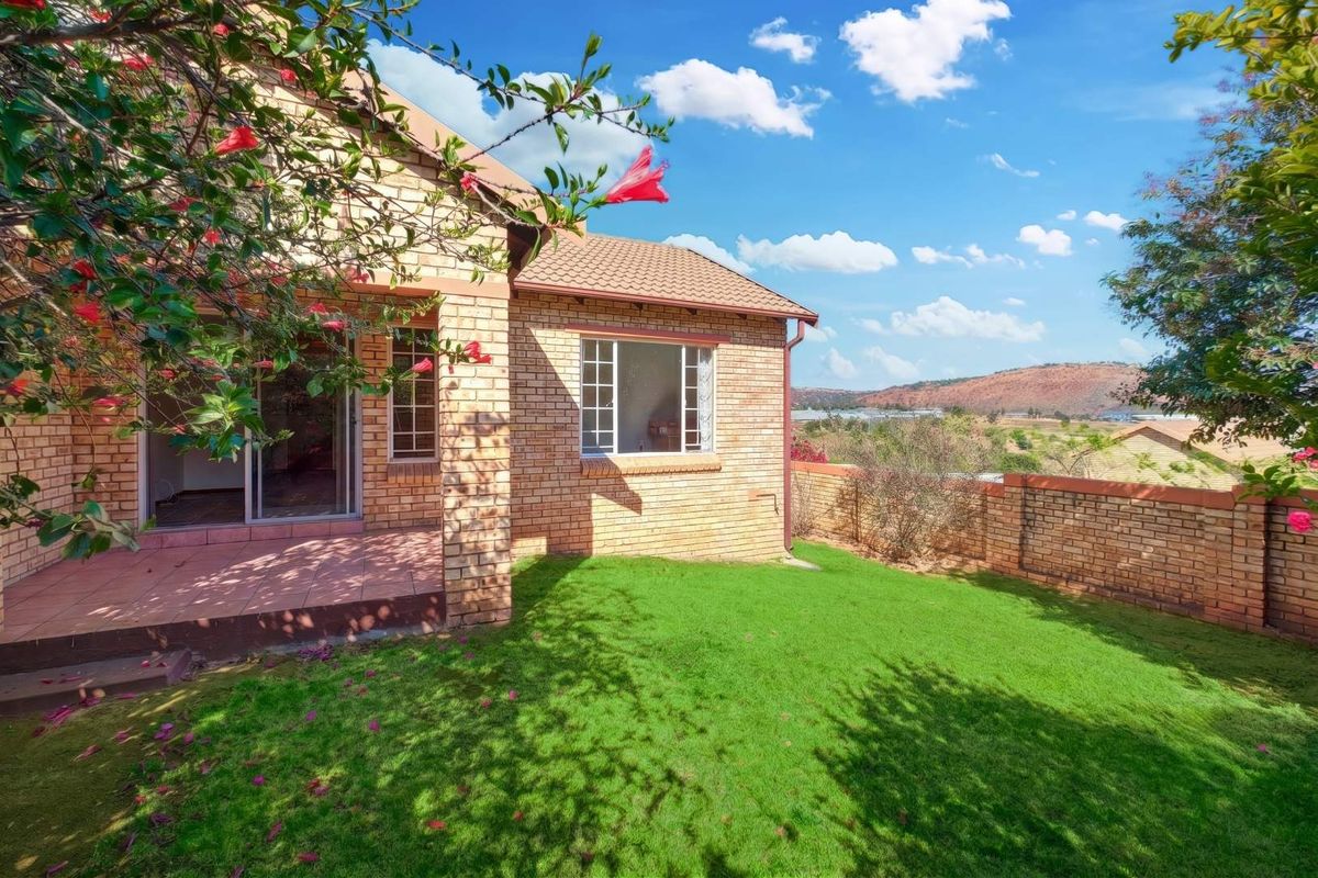 A rear view of the townhouse featuring a brick facade, a covered patio area, and a private garden with scenic landscape views.