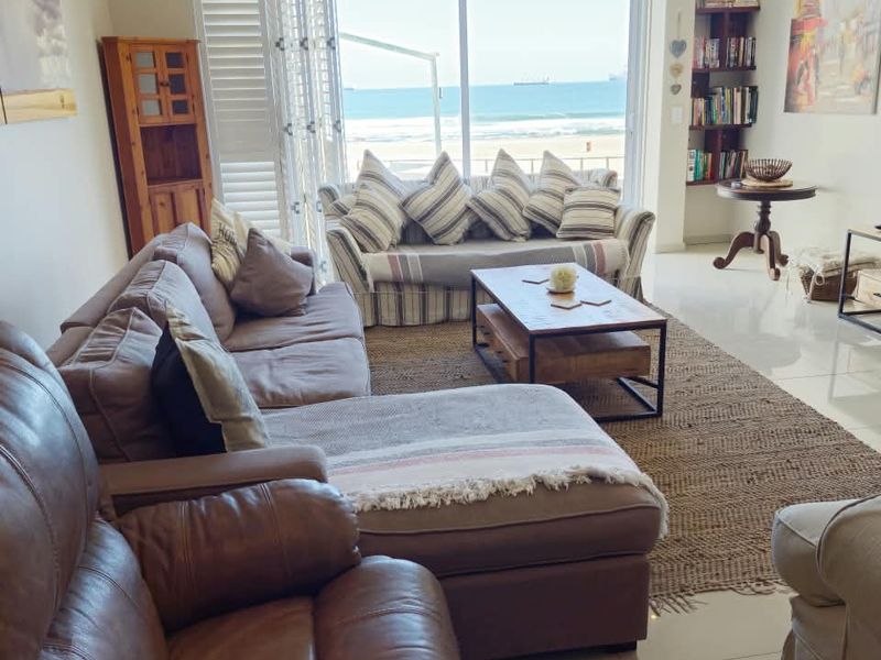 Spacious living room featuring large sliding glass doors that offer direct ocean views and abundant natural light, complemented by neutral tiled flooring.
