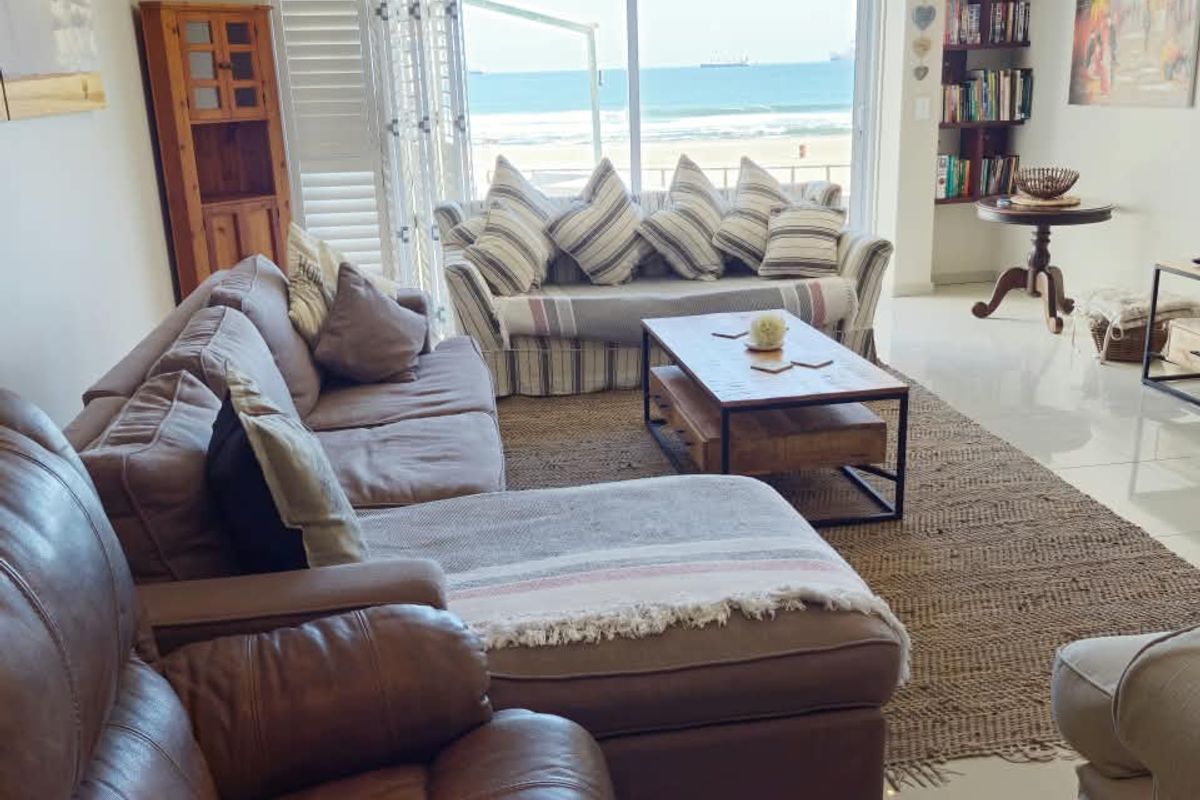 Spacious living room featuring large sliding glass doors that offer direct ocean views and abundant natural light, complemented by neutral tiled flooring.