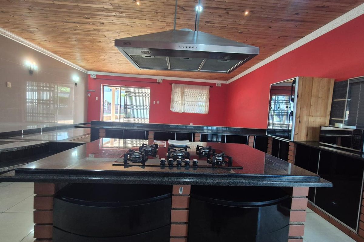 Spacious kitchen featuring a large central island with a gas hob, extractor fan, granite countertops, and a distinctive timber ceiling.