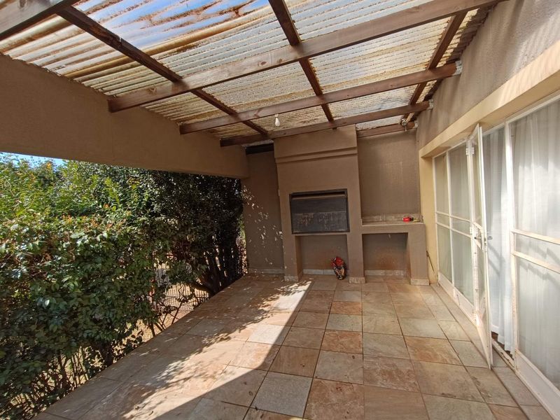 Covered outdoor patio featuring a built-in braai, tiled flooring, and direct access to the interior through sliding glass doors.