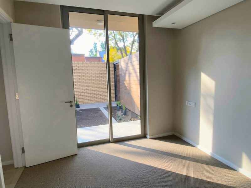 A bright, empty bedroom featuring neutral carpeting, a recessed ceiling detail, and a large sliding glass door providing direct access to a private outdoor area.