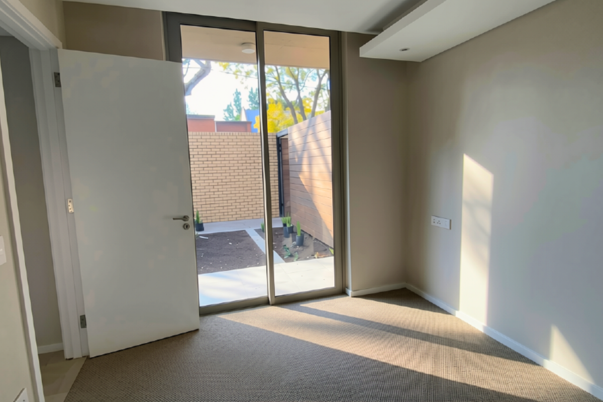 A bright, empty bedroom featuring neutral carpeting, a recessed ceiling detail, and a large sliding glass door providing direct access to a private outdoor area.