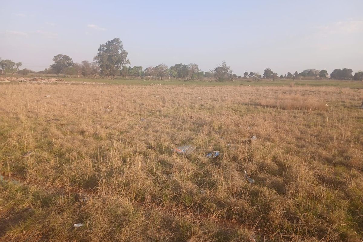 A wide-angle view of an undeveloped, vacant residential plot featuring dry grassland and scattered vegetation.