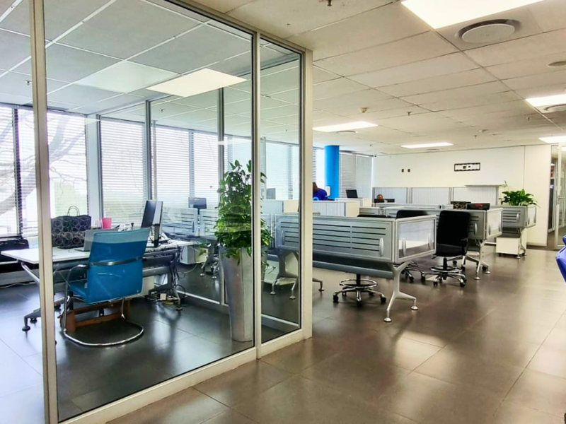 Open-plan office space featuring glass-partitioned private offices, suspended ceilings with recessed lighting, and durable tiled flooring throughout.