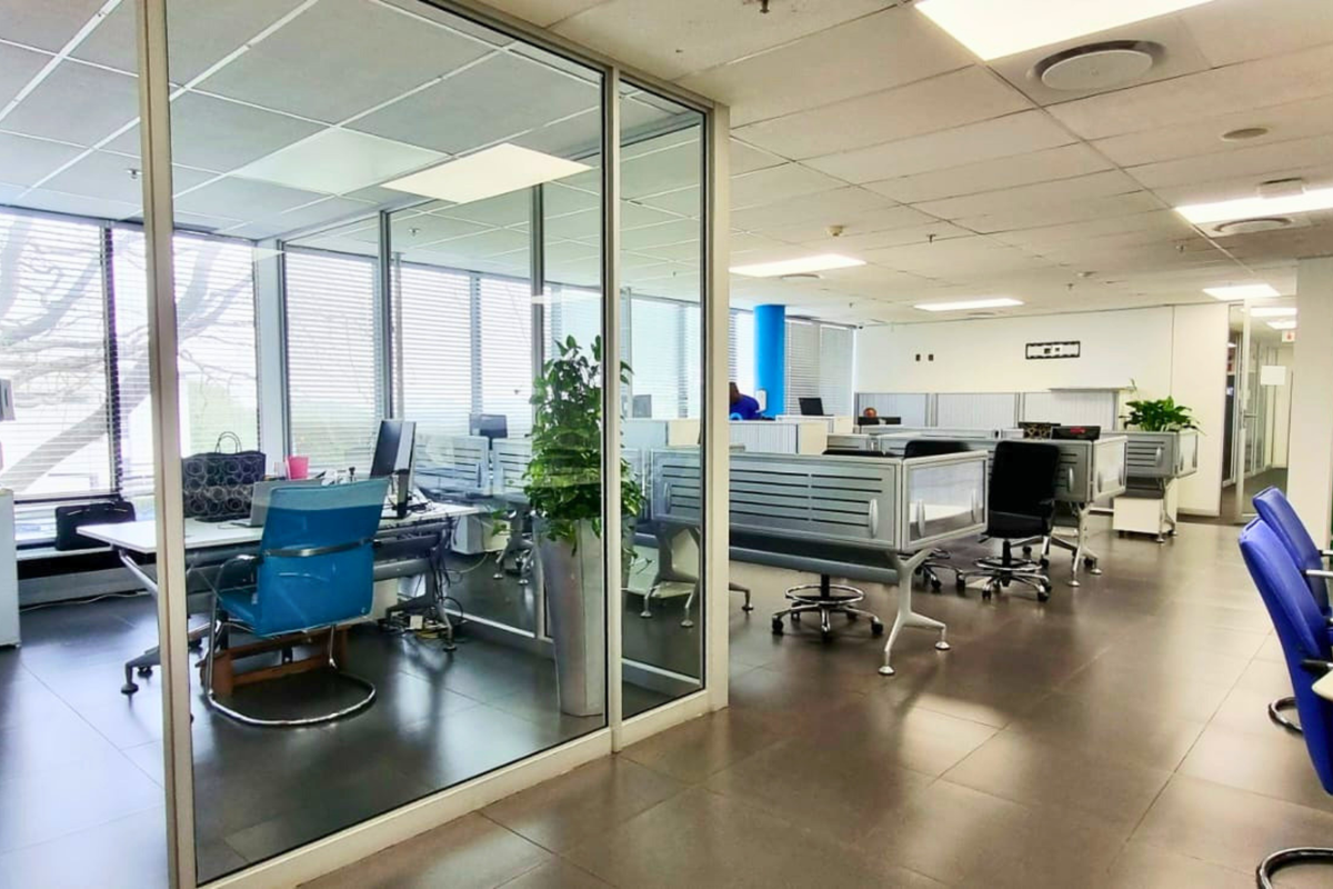 Open-plan office space featuring glass-partitioned private offices, suspended ceilings with recessed lighting, and durable tiled flooring throughout.