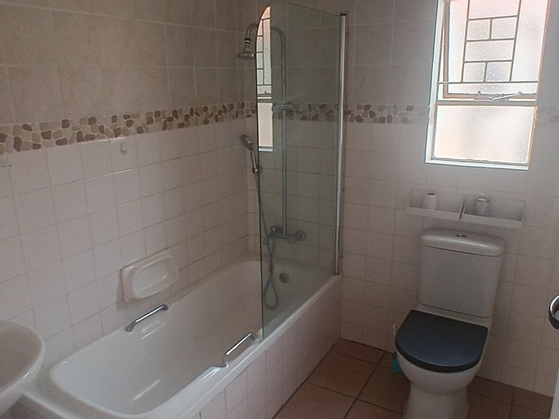 A functional bathroom featuring a bathtub with a glass shower screen, pedestal basin, toilet, and neutral tiled finishes throughout.