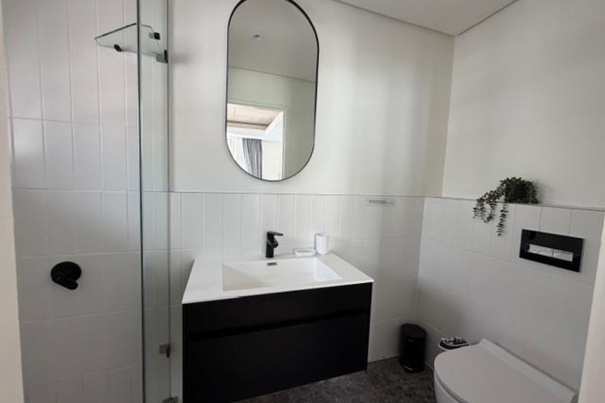 Modern bathroom featuring a floating vanity, wall-mounted toilet, glass-enclosed shower, and contemporary black fixtures.