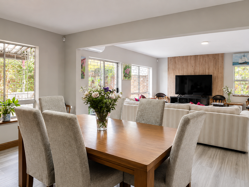 Spacious open-plan living and dining area featuring light laminate flooring, a timber feature wall, and large windows with security bars.