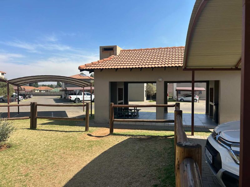 A view of the rear exterior featuring a covered patio area with a built-in braai, timber fencing, and adjacent carport parking.