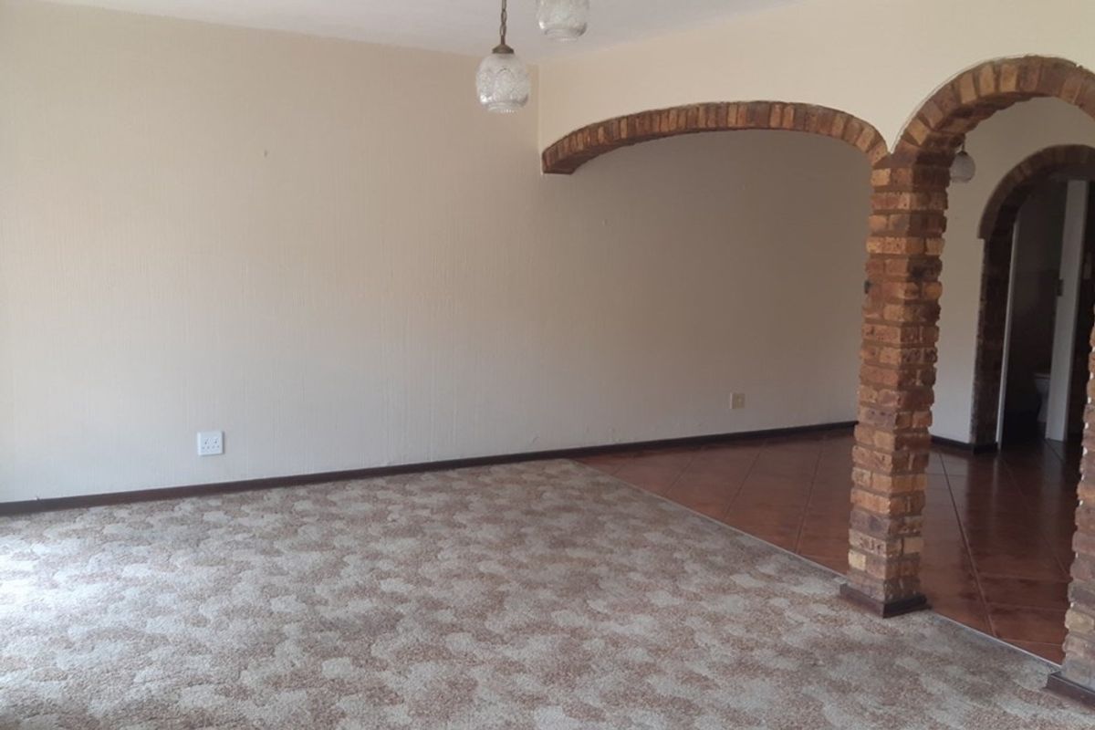 An empty living area featuring a distinctive brick archway, carpeted flooring, and transition to a tiled space, offering a blank canvas for renovation.