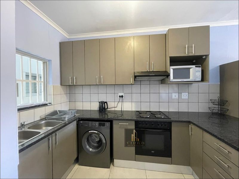 A functional kitchen featuring modern taupe cabinetry, granite countertops, a double basin sink, and integrated appliances including an oven, hob, and extractor fan.