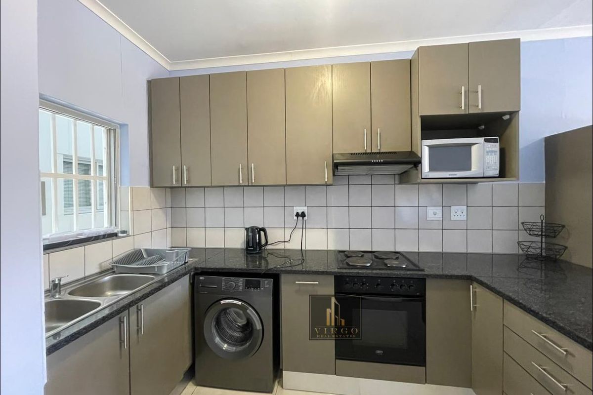 A functional kitchen featuring modern taupe cabinetry, granite countertops, a double basin sink, and integrated appliances including an oven, hob, and extractor fan.