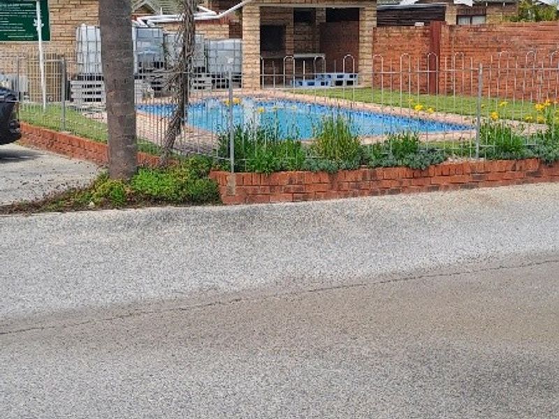 Outdoor pool area featuring a swimming pool, brick boundary wall, and a covered structure, viewed from the street.