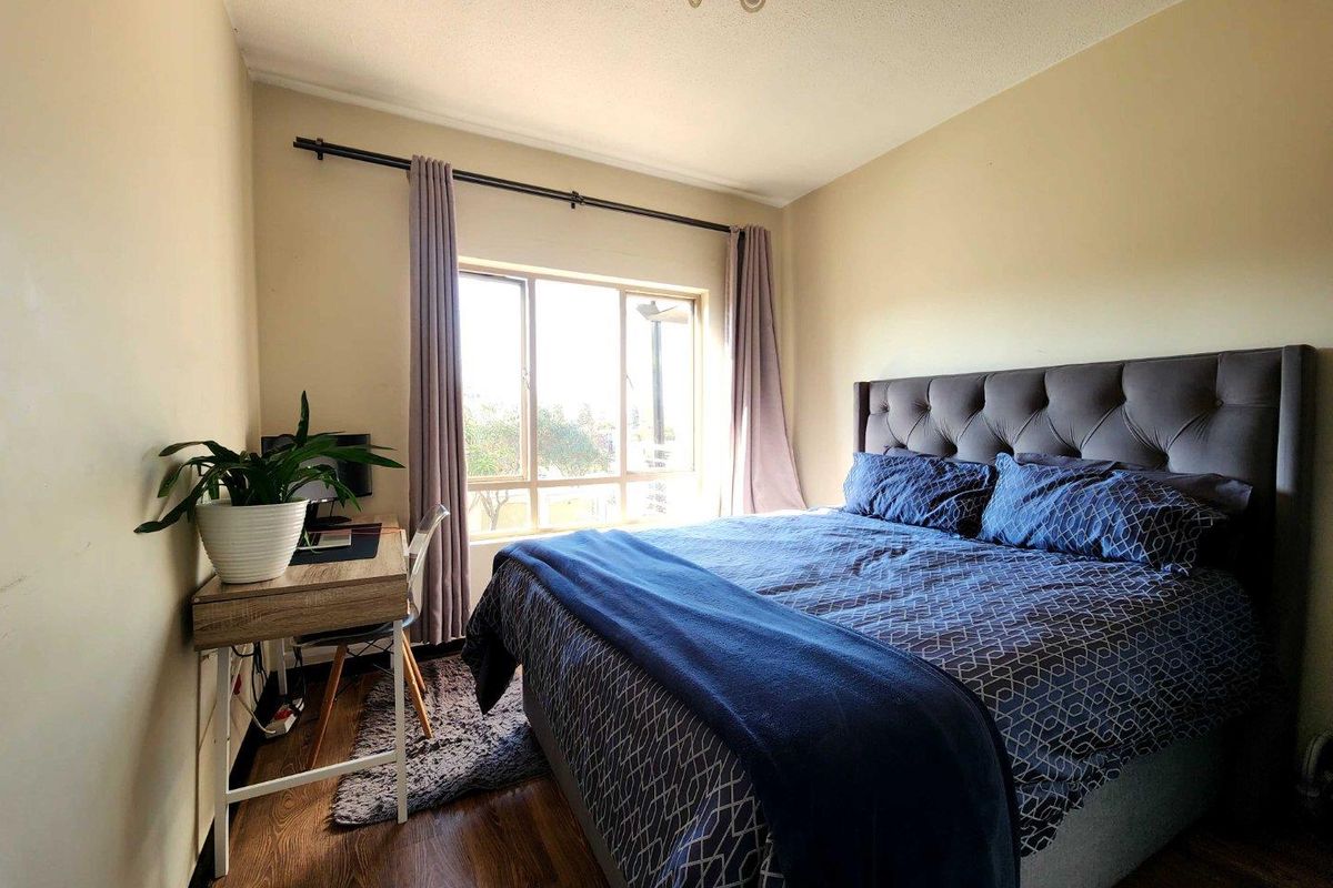 A bedroom featuring wood-look flooring, a large window providing natural light, and a ceiling-mounted light fixture.