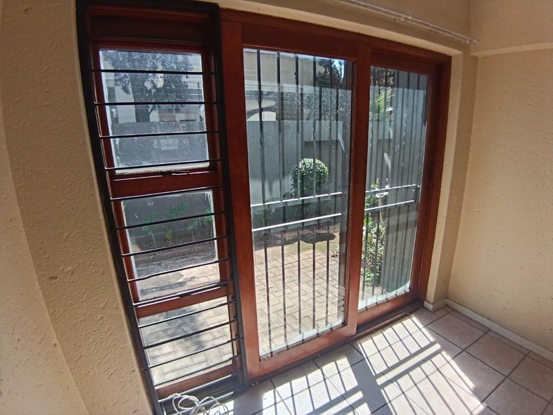 A covered patio area featuring tiled flooring and wooden sliding doors with integrated security bars, providing access to the outdoor space.