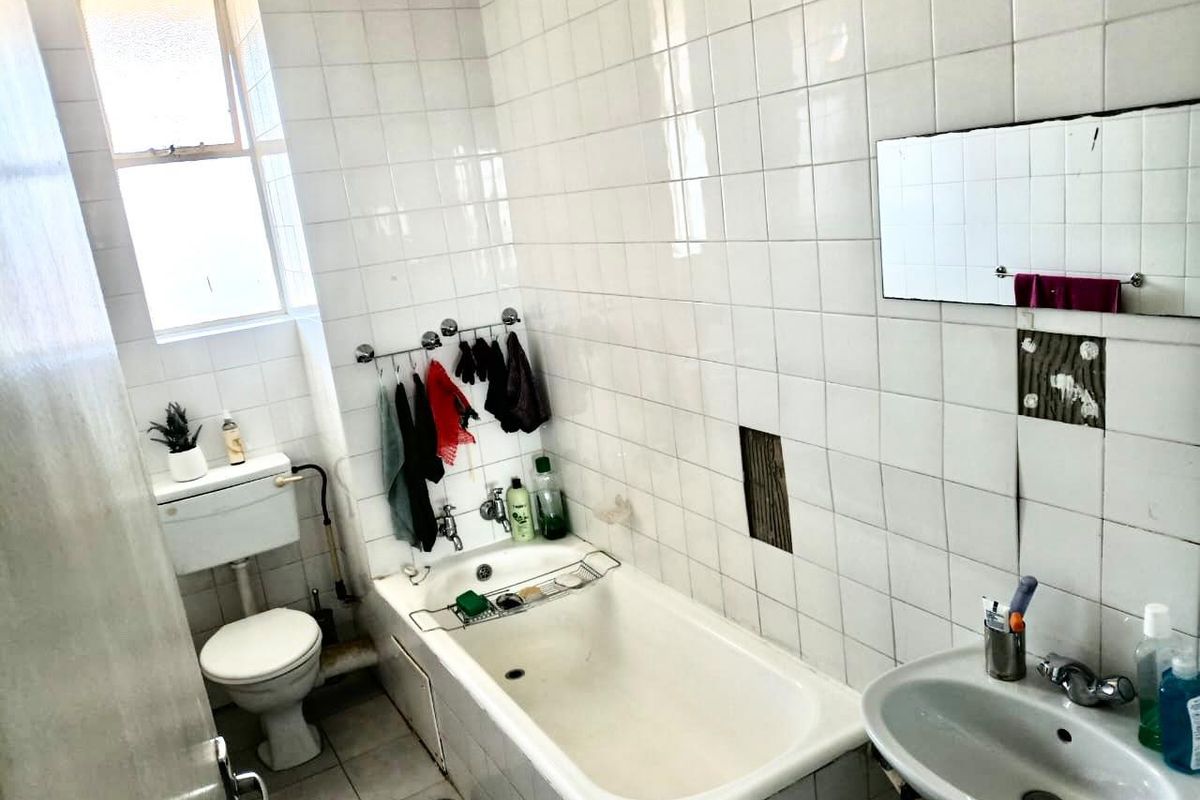 A dated bathroom featuring a bathtub, pedestal basin, and toilet, with white wall tiling and visible areas of missing or damaged tiles.