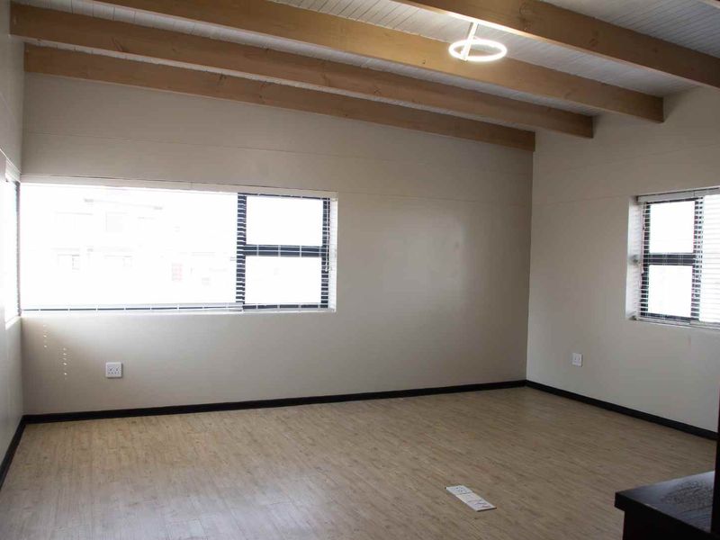 A bright, empty living area featuring exposed timber ceiling beams, modern laminate flooring, and large windows providing ample natural light.
