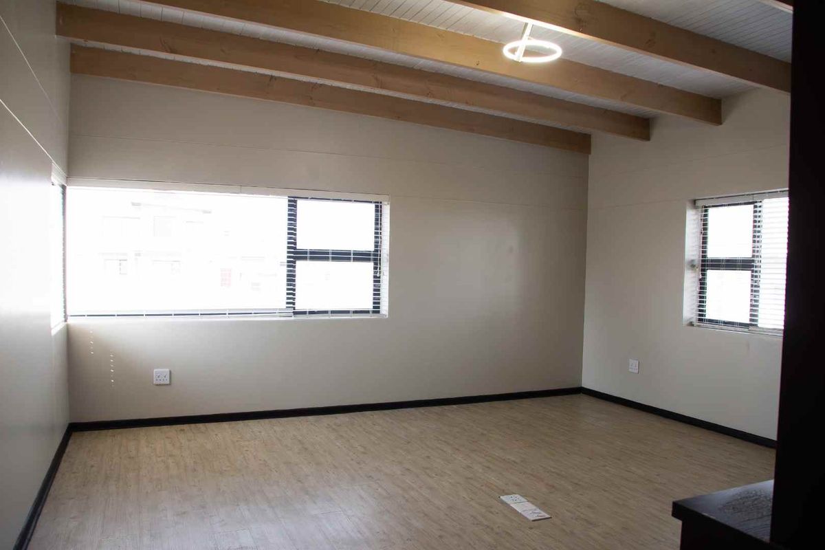 A bright, empty living area featuring exposed timber ceiling beams, modern laminate flooring, and large windows providing ample natural light.
