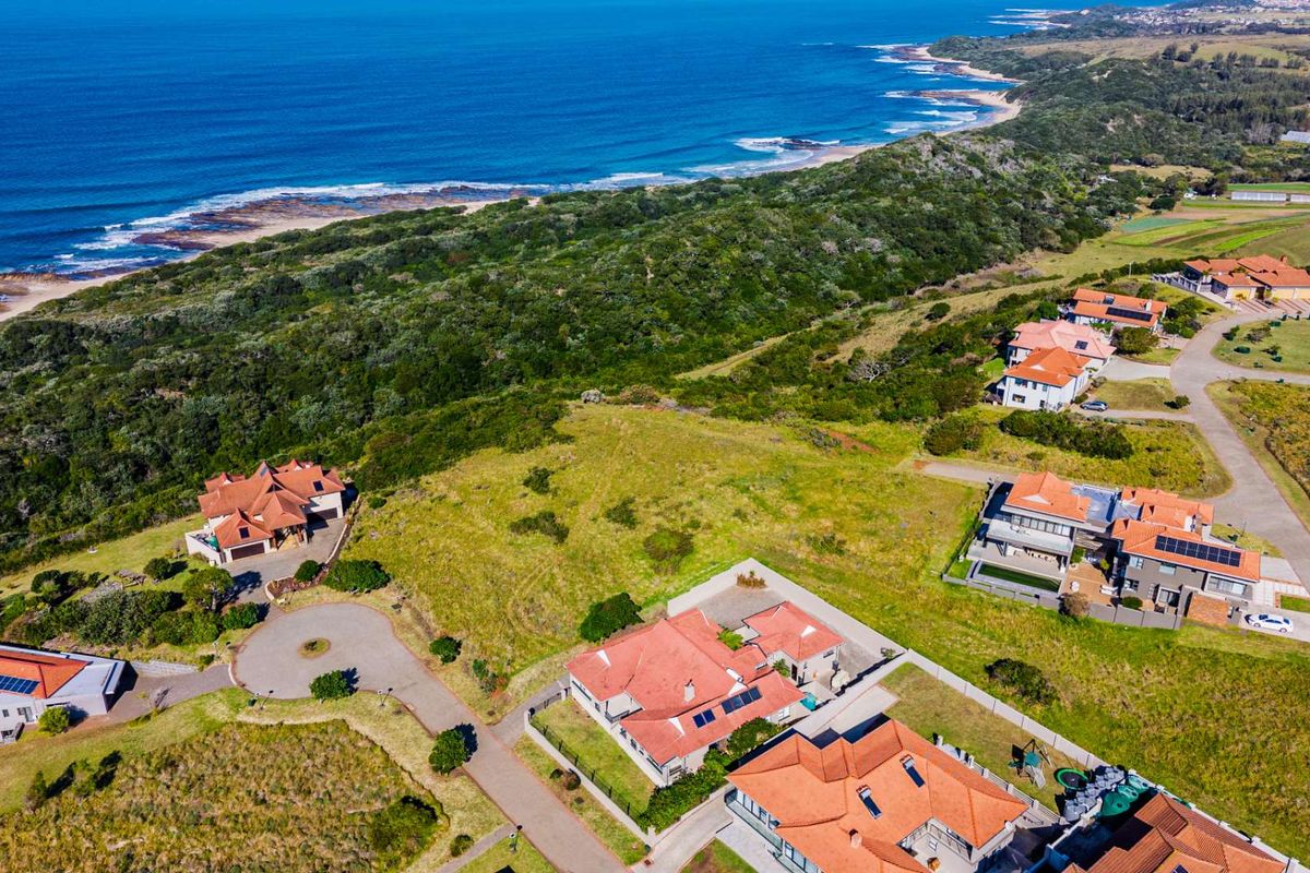 An aerial view of a coastal residential estate featuring established homes, paved roads, and expansive natural green space overlooking the ocean.
