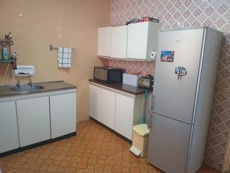 A functional kitchen featuring built-in cabinetry, laminate countertops, and a stainless steel sink, currently showcasing dated finishes and wall coverings.