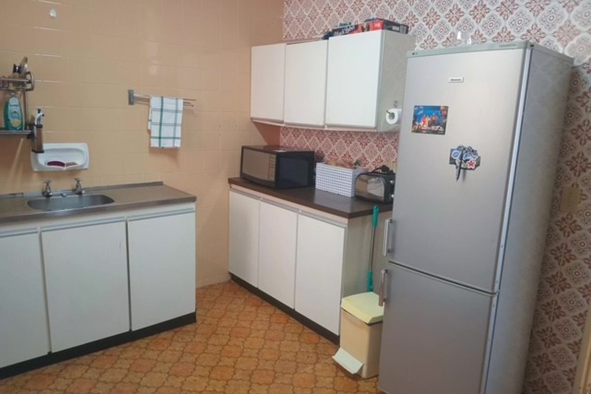 A functional kitchen featuring built-in cabinetry, laminate countertops, and a stainless steel sink, currently showcasing dated finishes and wall coverings.