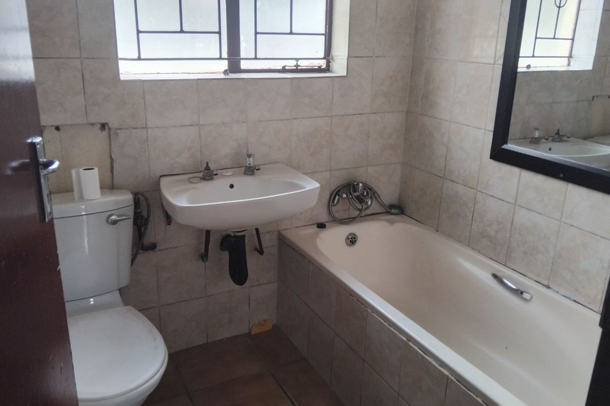 A dated bathroom featuring a standard bathtub, wall-mounted basin, and toilet with tiled walls and flooring.