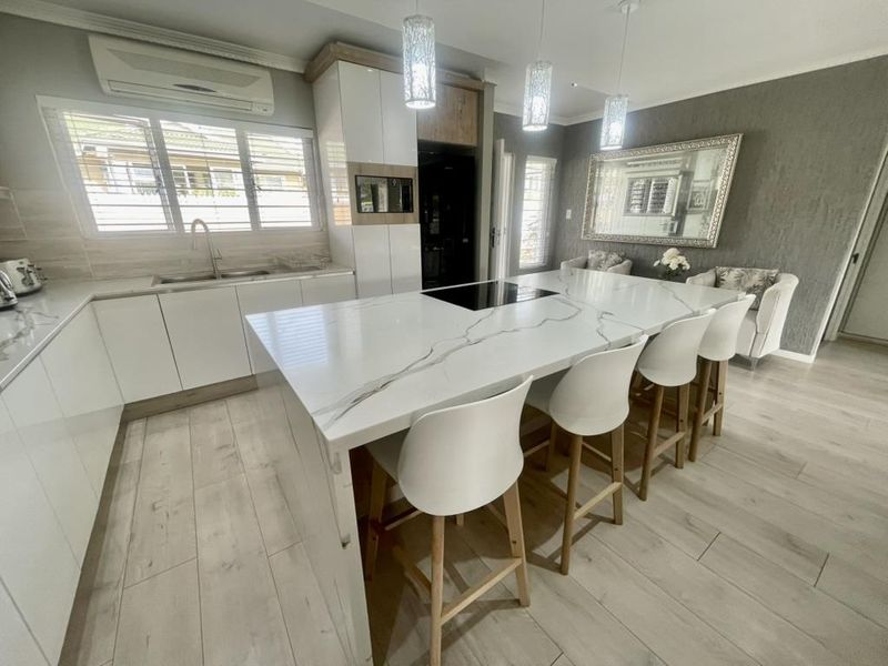 Modern kitchen featuring a large quartz-topped island with integrated cooktop, sleek white cabinetry, and high-end finishes throughout.