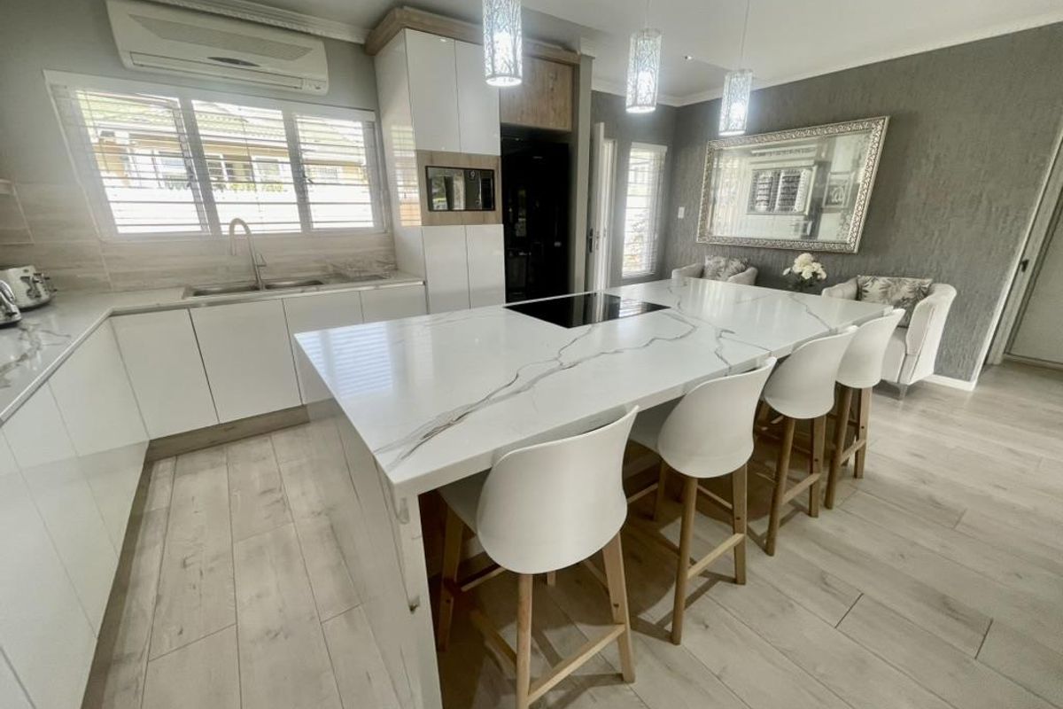 Modern kitchen featuring a large quartz-topped island with integrated cooktop, sleek white cabinetry, and high-end finishes throughout.