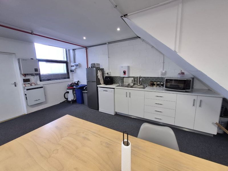 A functional office kitchenette featuring white cabinetry, a stainless steel sink, tiled backsplash, and integrated solar power infrastructure.