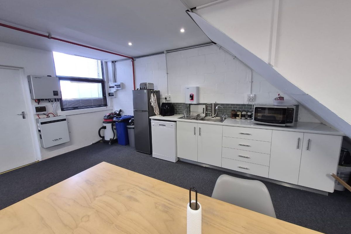 A functional office kitchenette featuring white cabinetry, a stainless steel sink, tiled backsplash, and integrated solar power infrastructure.