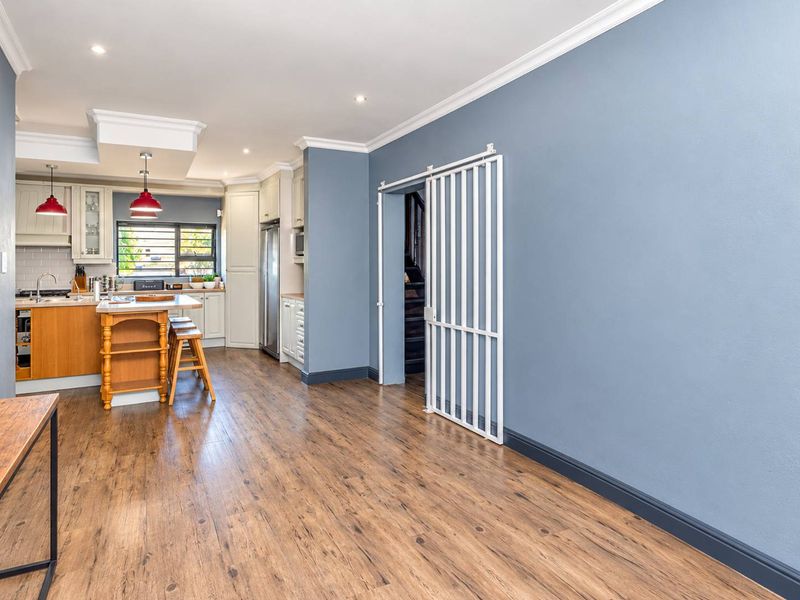 Open-plan kitchen and living area featuring modern cabinetry, a central island, laminate flooring, and a sliding security gate leading to the staircase.