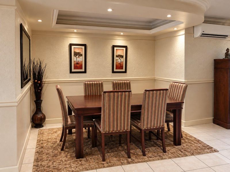 A well-maintained dining area featuring a recessed ceiling with downlights, wainscoting, and a wall-mounted air conditioning unit.