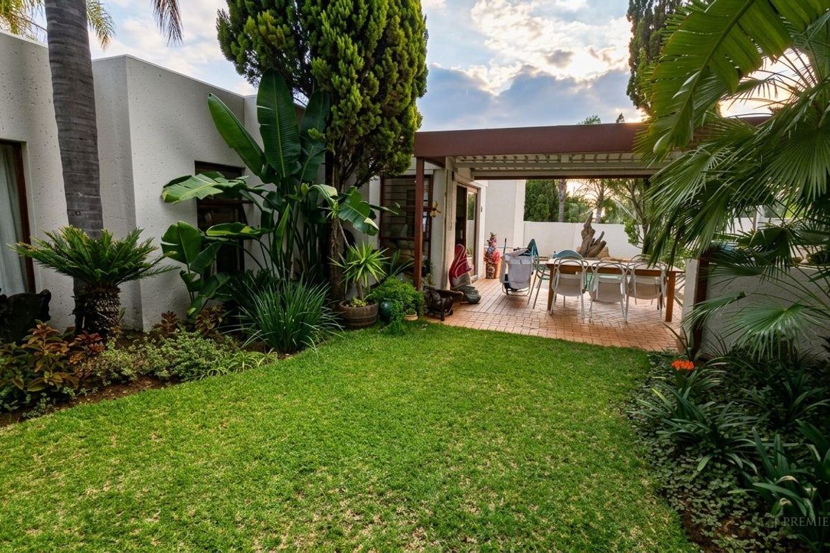 A well-maintained rear garden featuring a lush lawn, mature landscaping, and a covered patio area with brick paving.
