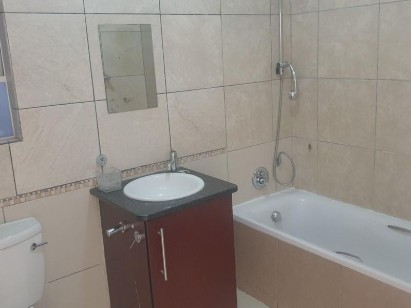 A functional bathroom featuring a built-in vanity with basin, a bathtub with shower mixer, and a standard toilet, finished with neutral wall tiling.