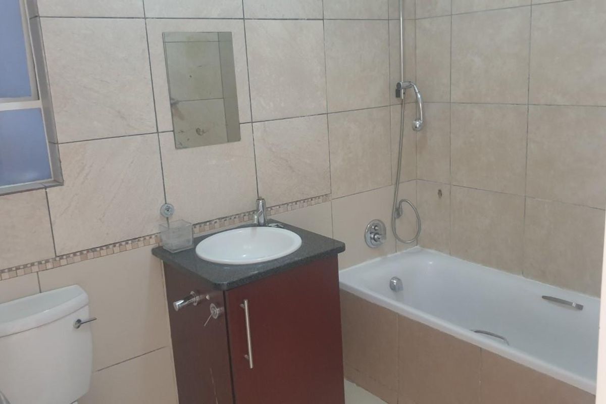 A functional bathroom featuring a built-in vanity with basin, a bathtub with shower mixer, and a standard toilet, finished with neutral wall tiling.