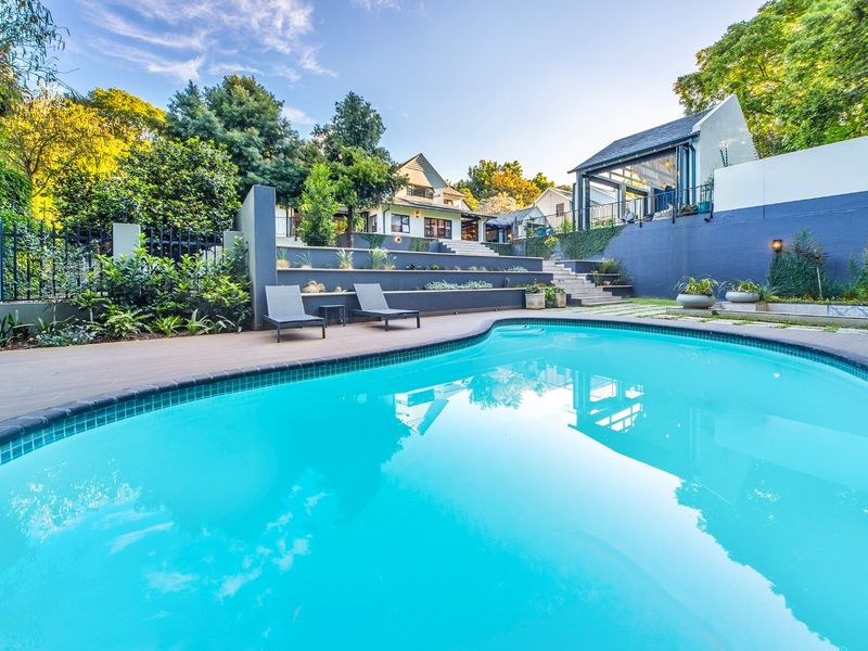 A beautifully landscaped outdoor pool area featuring tiered retaining walls, stone steps, and a well-maintained swimming pool set against a lush garden backdrop.