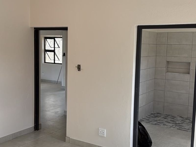 An empty bedroom featuring neutral tiled flooring, clean walls, and direct access to an en-suite bathroom with a tiled shower area.