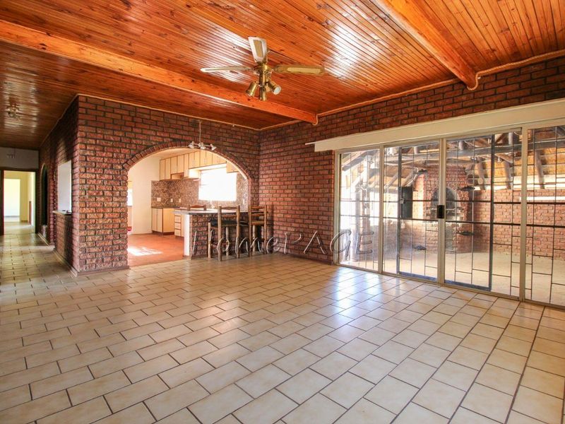 Spacious open-plan living area featuring exposed brick walls, timber ceiling, and large sliding glass doors leading to an adjacent room.