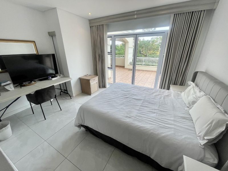 Spacious bedroom featuring large format floor tiles, recessed lighting, and a sliding glass door providing direct access to a private balcony.