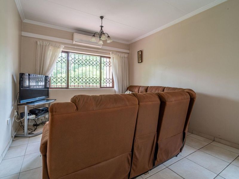 A comfortable living room featuring tiled flooring, a split-system air conditioner, and a window fitted with a security gate.