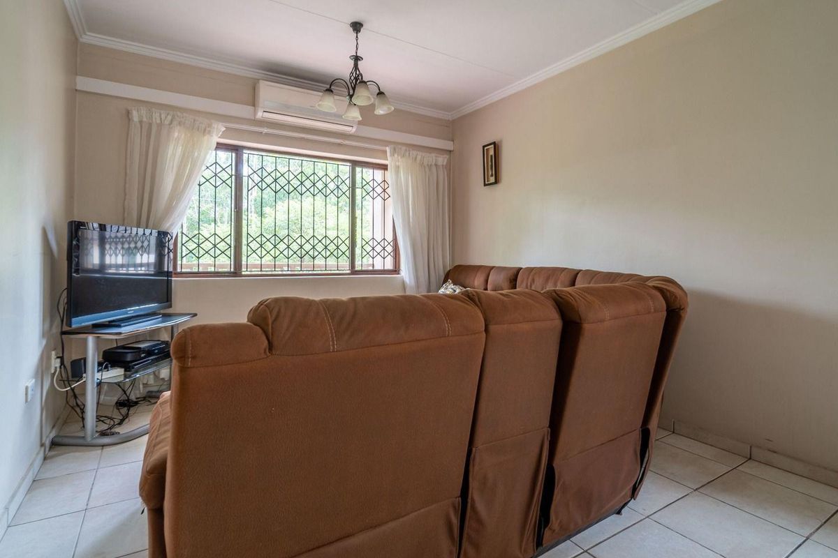 A comfortable living room featuring tiled flooring, a split-system air conditioner, and a window fitted with a security gate.