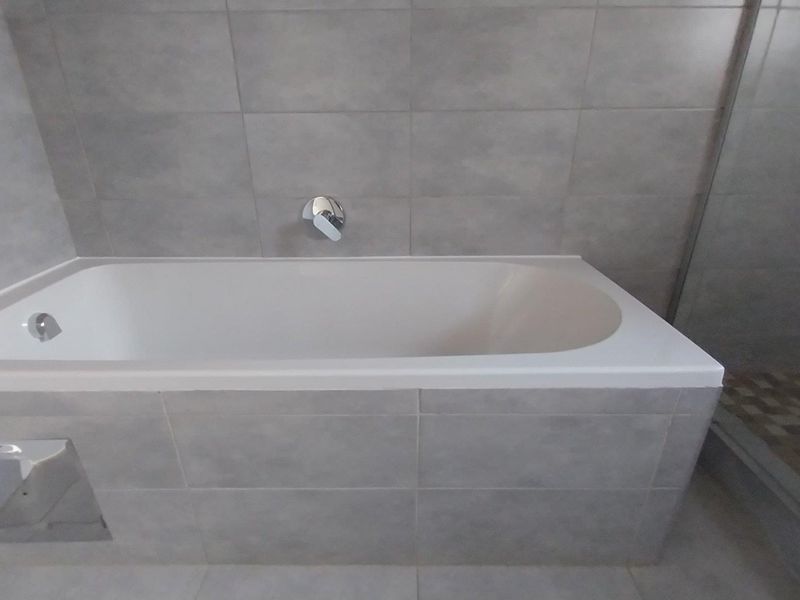 A modern bathroom featuring a built-in bathtub with wall-mounted mixer tap and neutral grey wall and floor tiling.