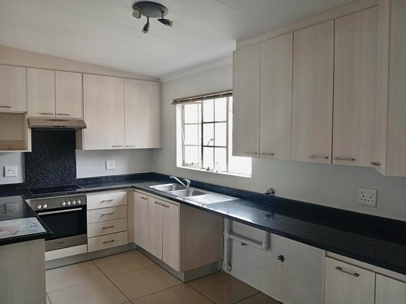 A functional kitchen featuring light wood-finish cabinetry, dark granite countertops, built-in oven and hob, and tiled flooring.