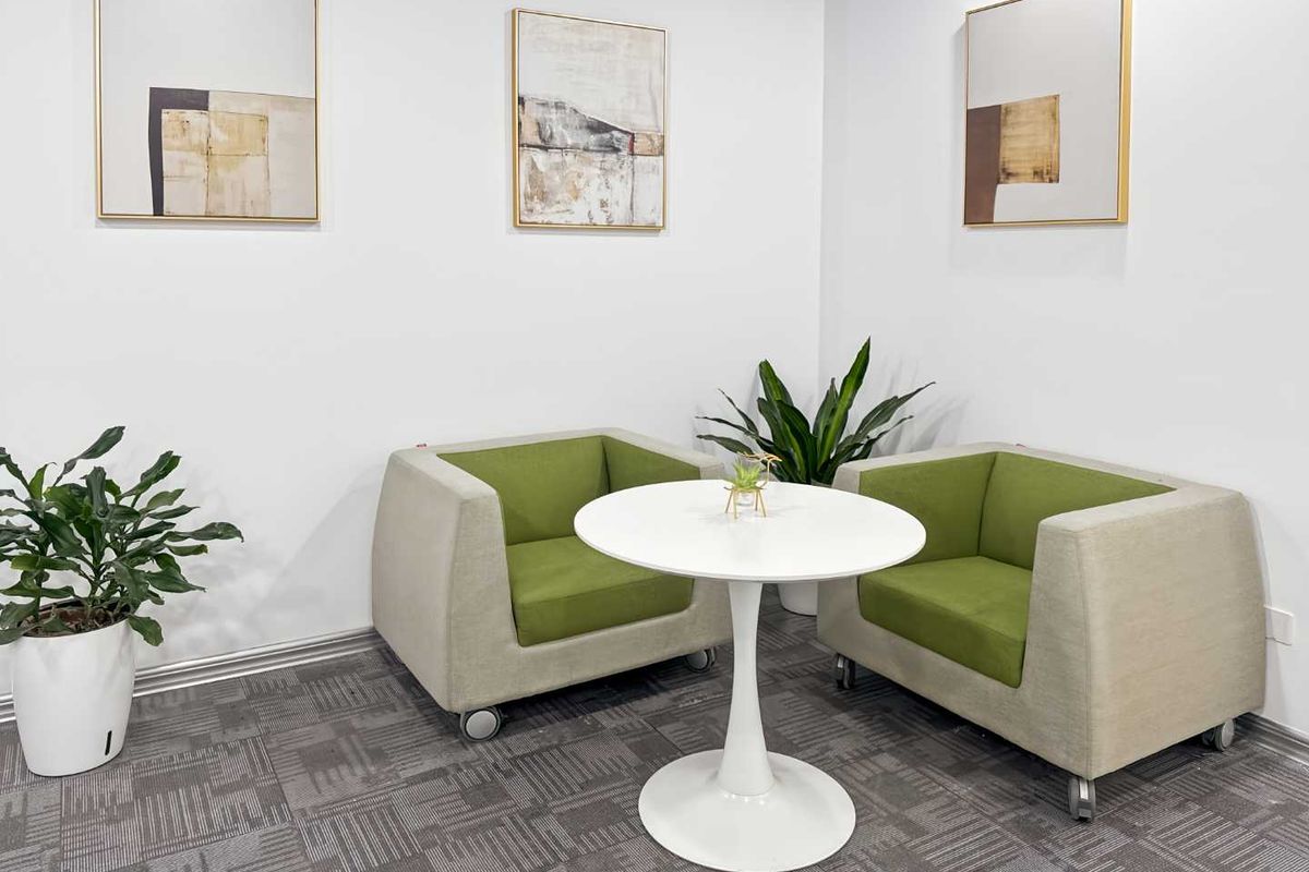 A clean and well-maintained office breakout area featuring neutral carpet flooring and white walls, suitable for professional meetings or casual workspace use.