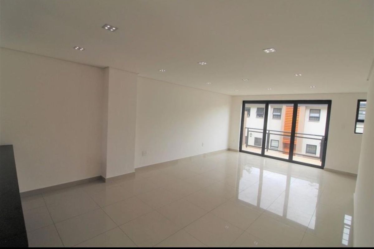A bright, open-plan living area featuring polished porcelain floor tiles, recessed downlighting, and large sliding glass doors leading to an outdoor balcony.
