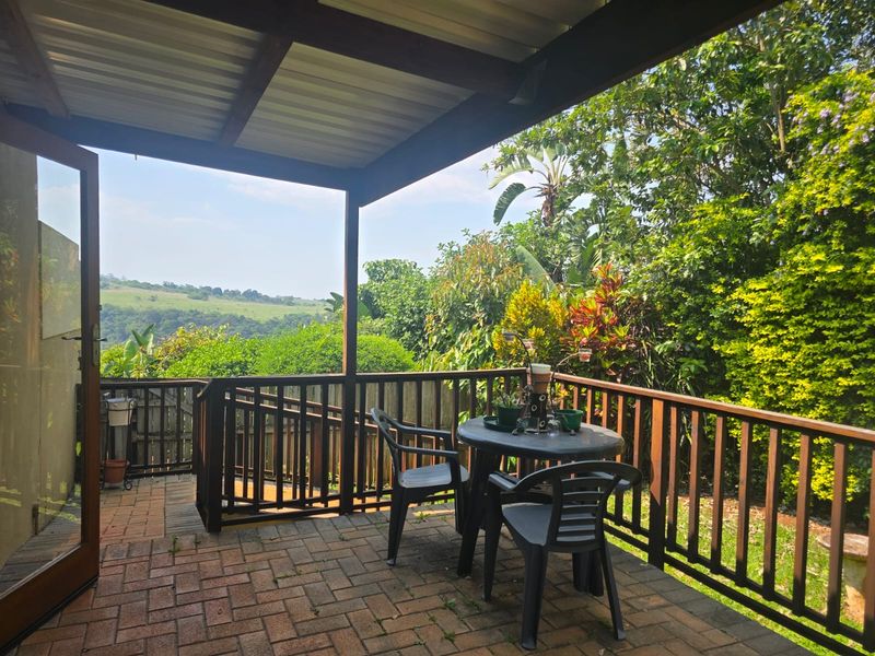 A covered outdoor patio featuring paved flooring and a timber balustrade, offering scenic views of the surrounding garden and landscape.